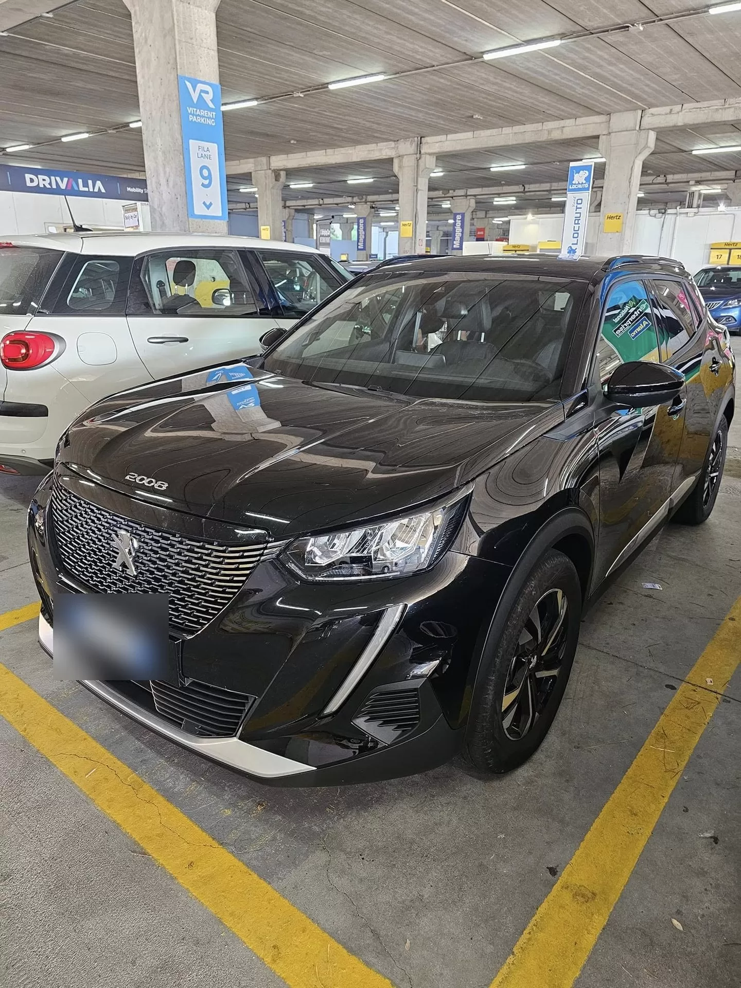 Locauto economy rental car in the Vitarent parking complex at Cagliari Airport, with Locauto, Hertz, Maggiore and Avis pick-up lanes visible