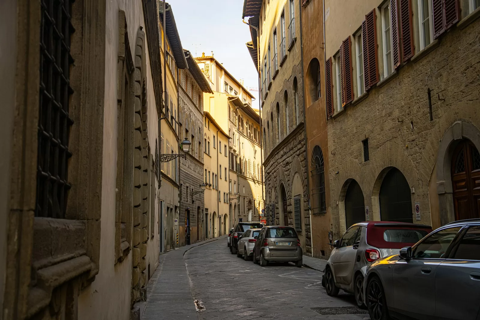 A narrow street in the Oltrarno district of Florence with cars parked along the old buildings