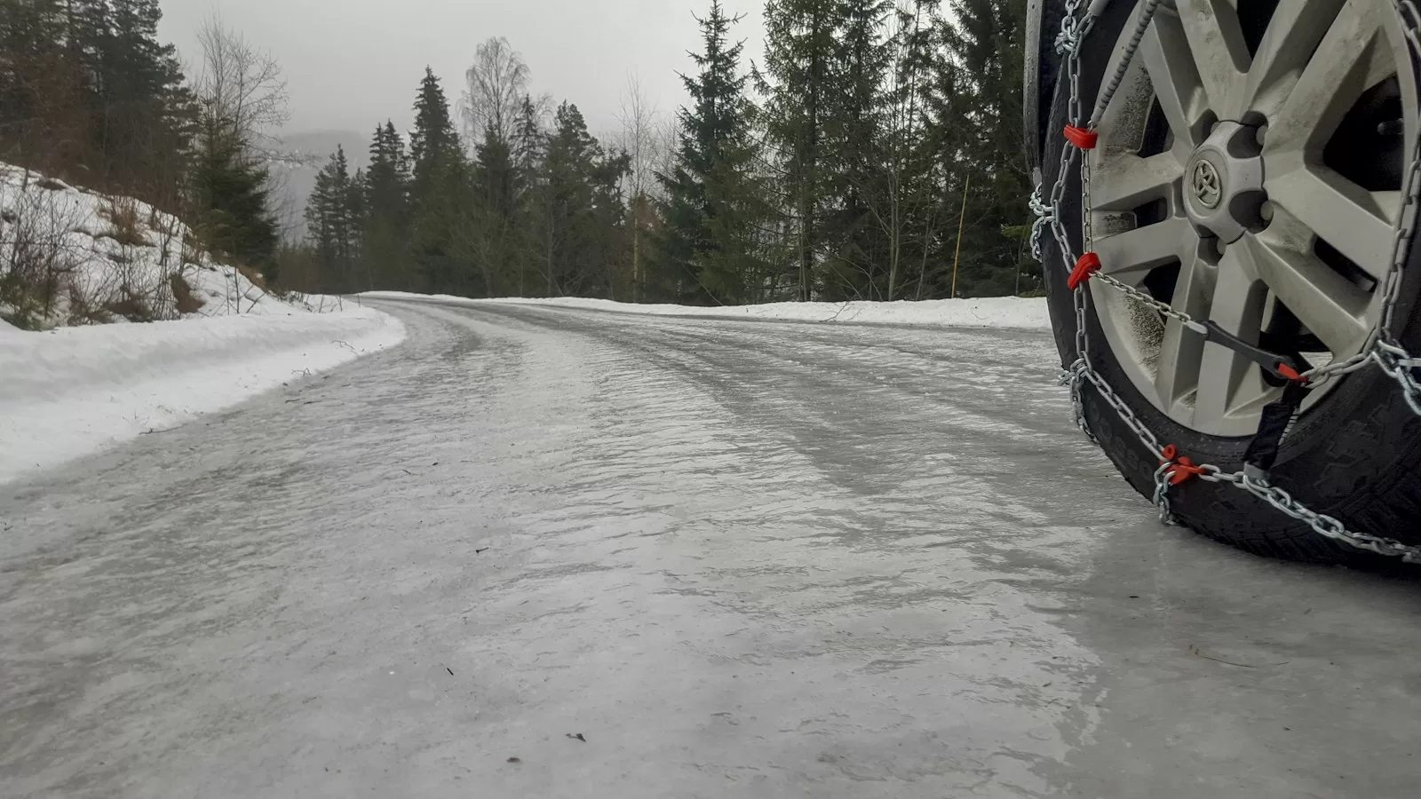 Snow chains fitted on a car wheel on an icy winter road